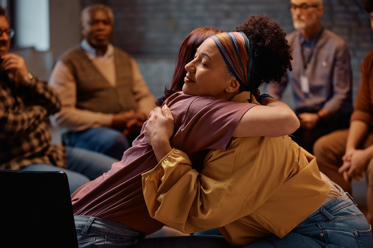 Group therapy participants hugging during mental health counseling at communicating center