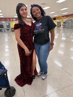 Two women smiling at camera in an indoor venue, one wearing a burgundy dress and one in a black shirt with jeans
