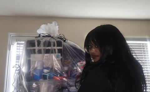 Woman with long black hair holding a clear plastic gift bag with white bow in front of a window
