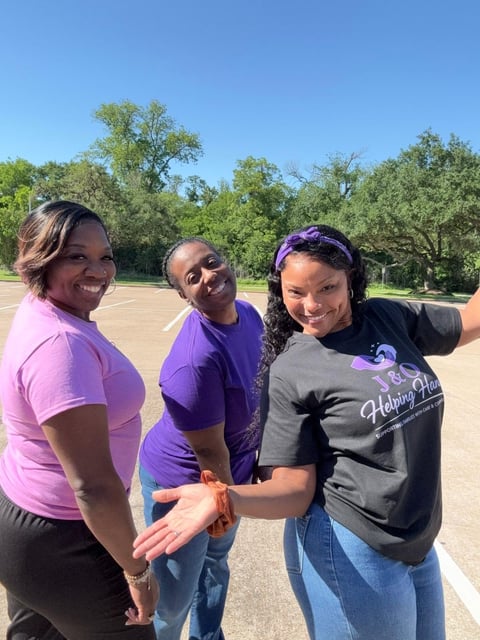 Three women smiling at camera outdoors in parking lot with purple awareness ribbons on wrists