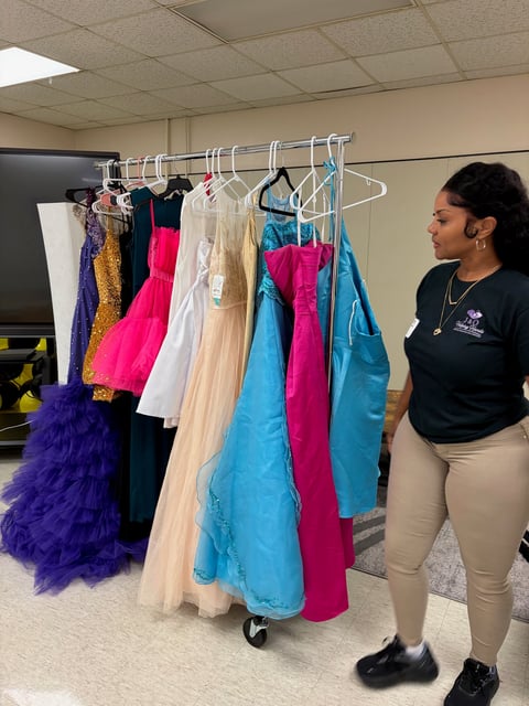Woman examining a clothing rack displaying colorful formal dresses in various colors including purple, pink, blue, and cream in an indoor setting