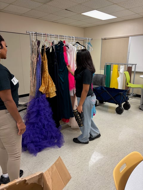 Two people browsing colorful formal dresses on clothing racks in a community wardrobe or thrift shop