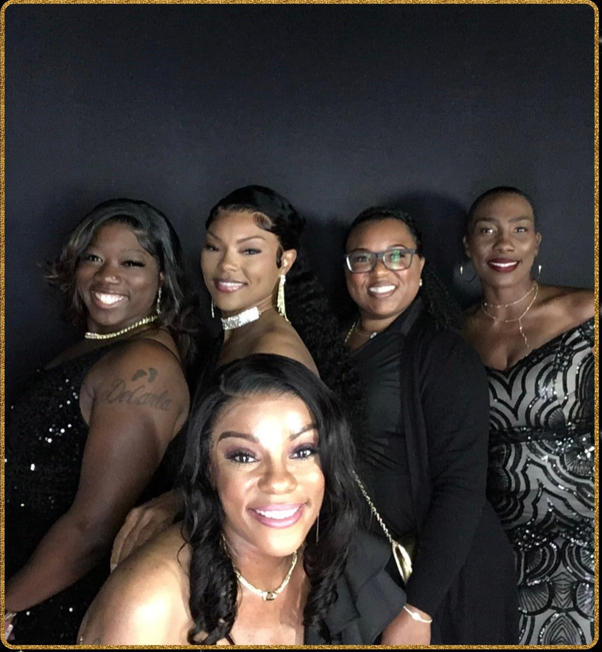 Five women smiling at camera in formal attire against dark background
